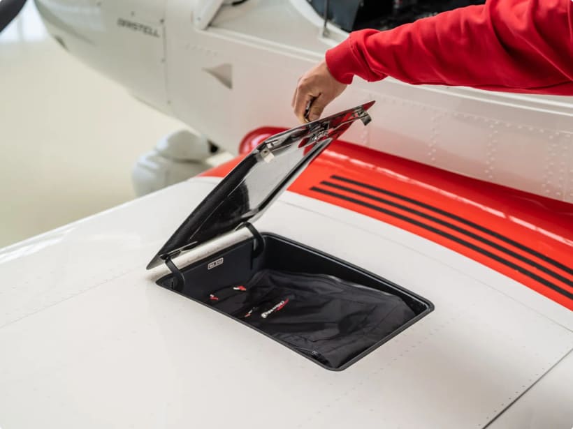 Open wing-root luggage locker on a red-and-white Bristell being loaded by hand.
