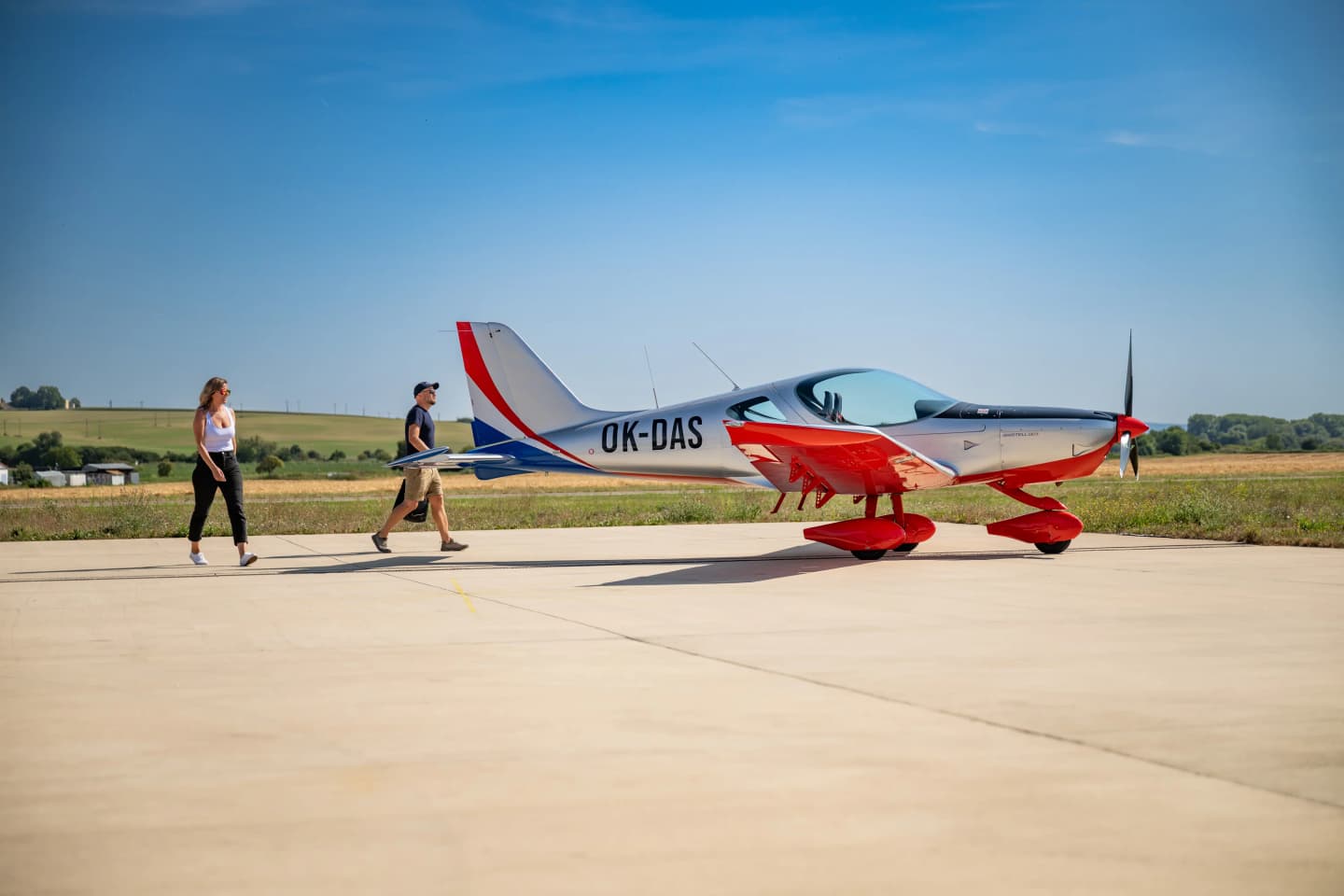 A couple walking across the apron to their silver and red Bristell B23