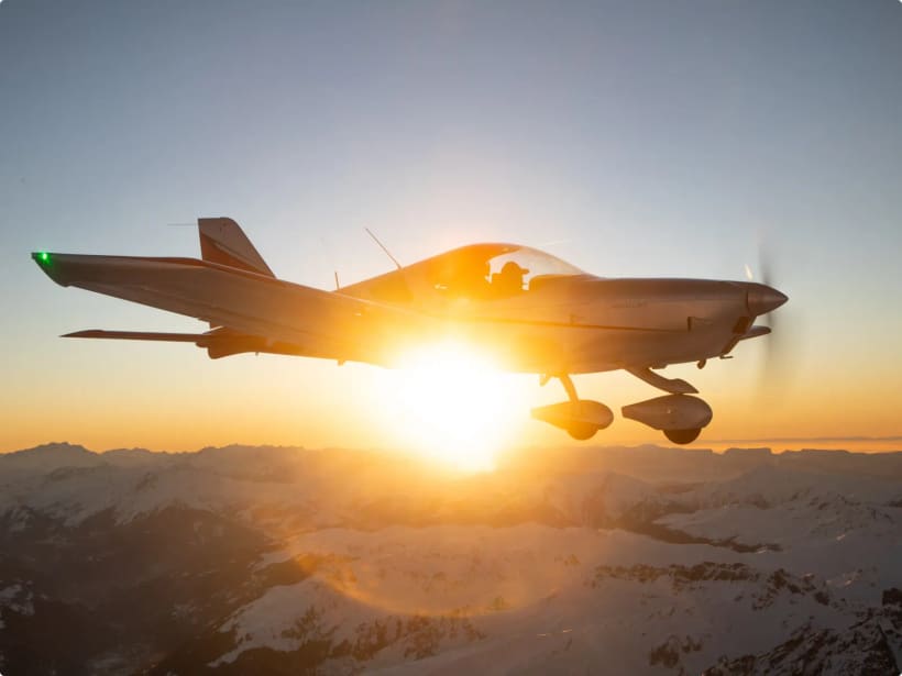 A Bristell silhouetted against a low sun over mountains, representing night-VFR flying.