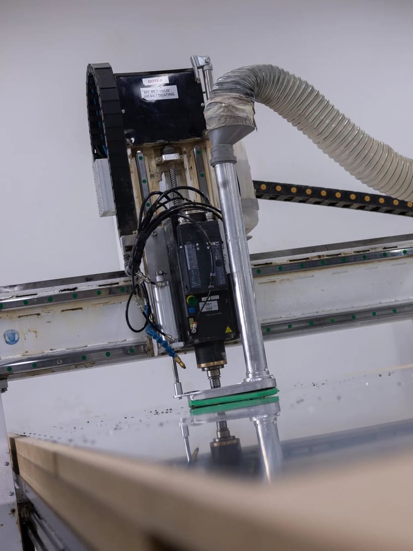 The cutting head and dust extraction hose of a gantry milling machine working an aluminium sheet in the Bristell machine shop