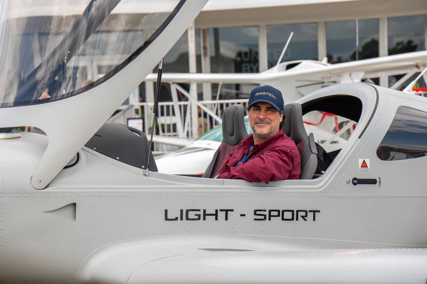 Bernardo Saviñon seated in the cockpit of his military-gray Bristell Classic, wearing a Bristell cap