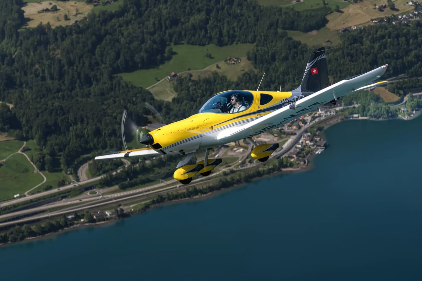 A Bristell B23 low-wing light aircraft in flight over a lake